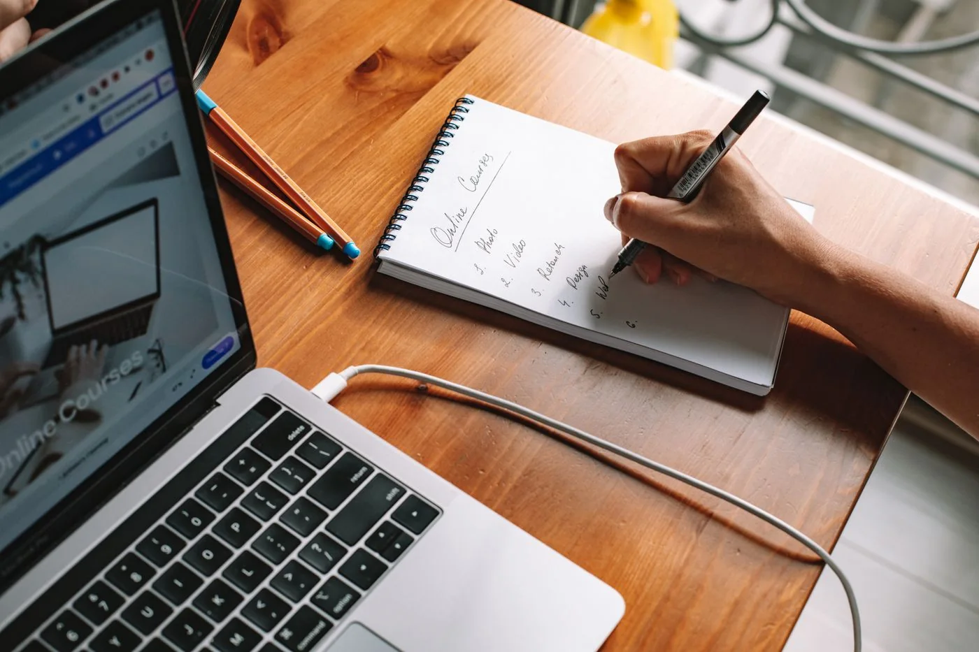 Person taking notes beside a laptop